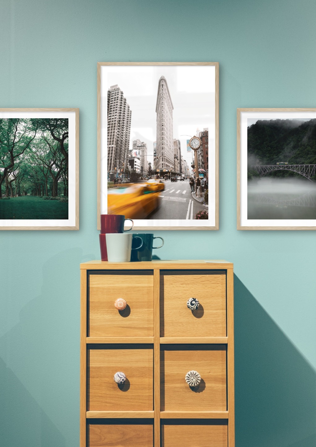 Tavelvägg med ramar i trä i storlekar 40x50 och 50x70 med posters med "Grönska och träd", "Gula taxibilar i stad" och "Tåg över bro"