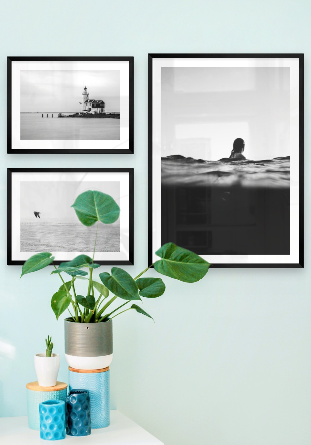 Tavelvägg med ramar i svart i storlekar 30x40 och 50x70 med posters med "Pir med byggnad", "Fåglar över havet" och "Person i vattnet"