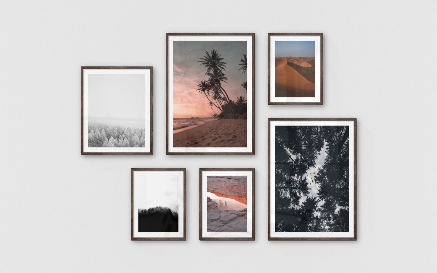 Tavelvägg med ramar i mörkt trä i storlekar 40x50, 50x70 och 30x40 med posters med "Trätoppar i vintern", "Strand i solnedgång", "Trätoppar och dimma", "Utsikt mellan klippor", "Trätoppar och fåglar" och "Öken"