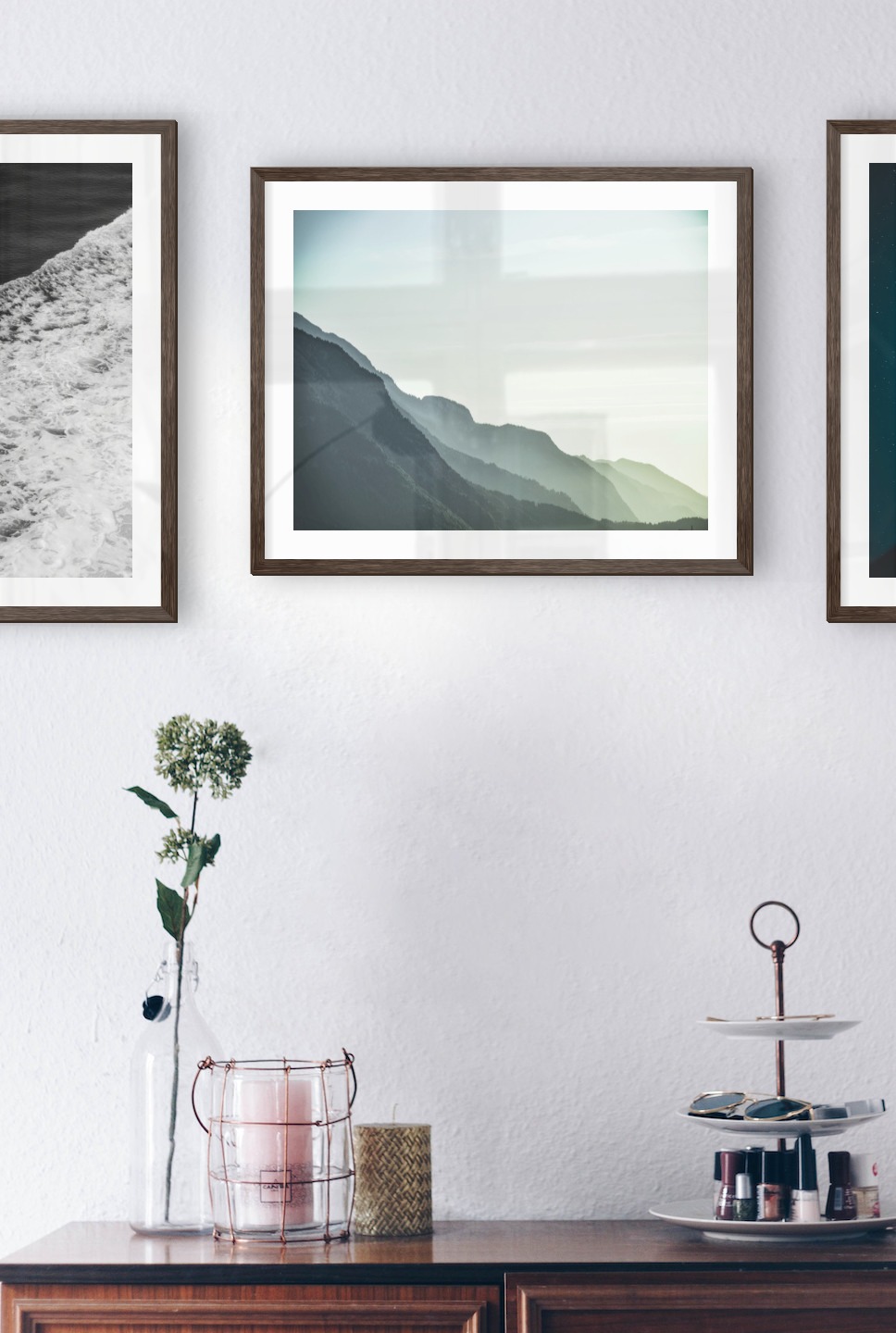 Tavelvägg med ramar i mörkt trä i storlekar 50x50 och 40x50 med posters med "Svall från vågor", "Dimmigt berg" och "Burk framför rymden"