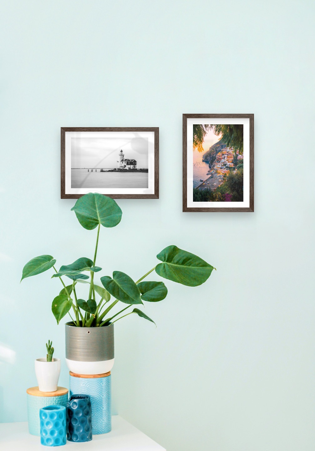 Tavelvägg med ramar i mörkt trä i storlekar 21x30 med posters med "Pir med byggnad" och "Stad vid havet"