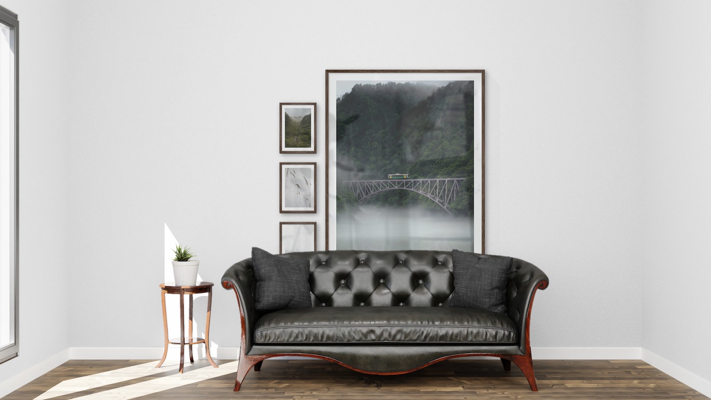 Tavelvägg med ramar i mörkt trä i storlekar 21x30 och 100x150 med posters med "Bäck i dal", "Vass i snön", "Dimmiga trätoppar" och "Tåg över bro"
